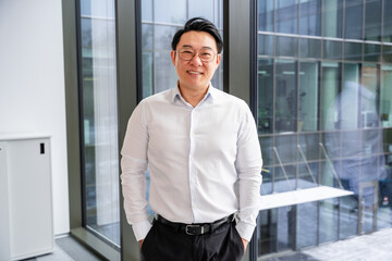 Successful professional standing by the window in a contemporary office building, dressed in...