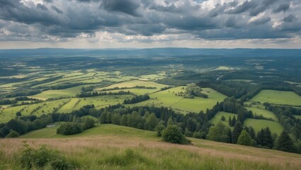 Fototapeta premium Panoramic View From Hilltop Overlooking Lush Meadows Forests And Fields Beneath Dramatic Cloudy Sky During Summer Hiking Adventure