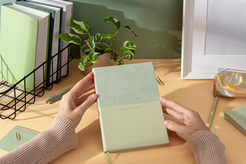 Women's hands show elegant lightgreen weekly planner with stationery, sticky notes, perfect for notes, sketches, and organizing thoughts.  Organized workspace, productive study setup.