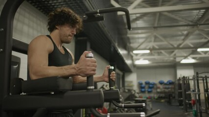 Athletic man gripping handles and performing hanging leg raises on Captain's chair during core workout in gym