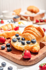 Delicious breakfast spread featuring buttery croissants topped with fresh strawberries and blueberries, served on a wooden board with butter, coffee, and fruit, creating a cozy