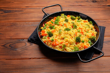 Tasty rice with vegetables in baking dish on wooden table, space for text