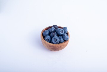 Close-up of fresh blueberries in a rustic wooden bowl, isolated on a clean white background. The vibrant berries highlight their natural texture, perfect for breakfast, desserts, and healthy snacks