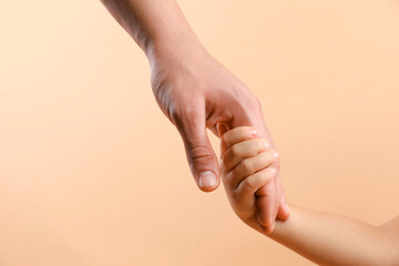 Father and child holding hands on beige background, closeup