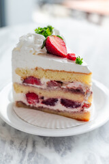 Close-up of a slice of strawberry shortcake with layers of sponge cake, whipped cream, and fresh strawberries, garnished with whipped topping, parsley, and sliced strawberries on a white plate