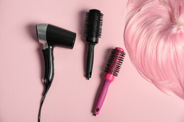 Stylish round brushes, hairdryer and lock of dyed hair on pink background, flat lay