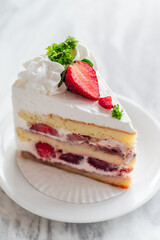 Close-up of a slice of strawberry shortcake with layers of sponge cake, whipped cream, and fresh strawberries, garnished with whipped topping, parsley, and sliced strawberries on a white plate