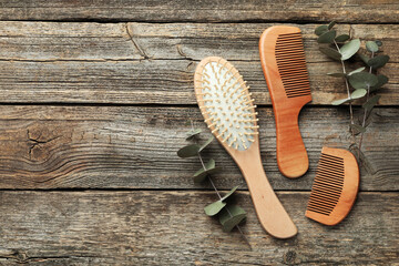Hair brush, combs and eucalyptus on wooden background, flat lay. Space for text