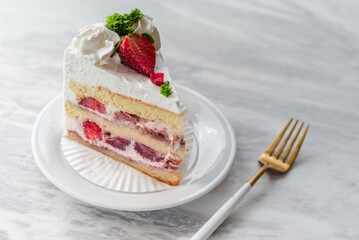 Slice of strawberry shortcake with layers of cream and fresh strawberries, garnished with whipped cream and parsley, served on a white plate with a gold fork on a marble table