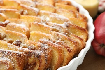 Delicious bread pudding with raisins, powdered sugar and apple on wooden table, closeup