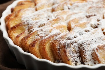 Delicious bread pudding with raisins and powdered sugar in dish, closeup