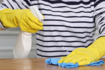 Woman using cleaning product while wiping wooden table with rag indoors, closeup