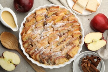 Delicious bread pudding with raisins, powdered sugar, cinnamon and apples on grey table, flat lay