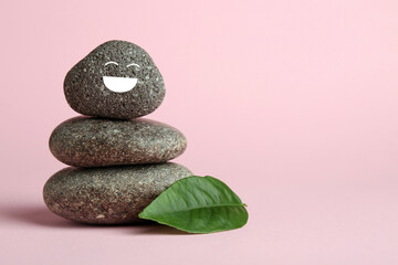 Stack of rocks with drawn smiley face on light pink background, space for text. Harmony and life...