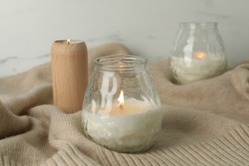 Burning soy wax candles and beige warm fabric on light table, closeup