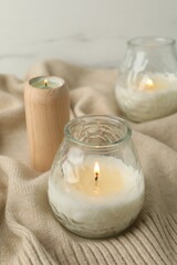 Burning soy wax candles and beige warm fabric on light table, closeup