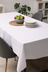 Table with white tablecloth, apples, plates and chairs in stylish room