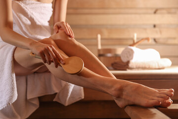 Woman massaging her leg with brush at sauna, closeup