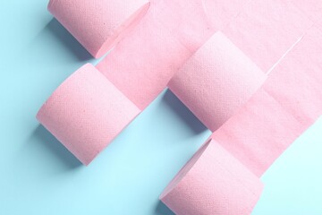 Pink toilet paper rolls on light blue background, top view