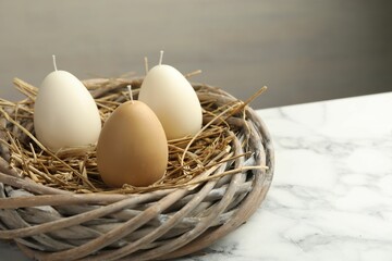 Egg-shaped candles in nest on white marble table, closeup. Easter decor