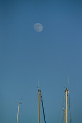 Fototapeta premium Sardinia, Alghero port, moon and masts of moored boats against the sky