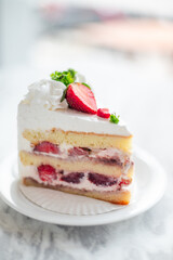 Close-up of a slice of strawberry shortcake with layers of sponge cake, whipped cream, and fresh strawberries, garnished with whipped topping, parsley, and sliced strawberries on a white plate