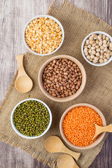 An assortment of legume products: chickpeas, mung beans, lentils, peas, beans in bowls on a cloth, burlap. Top view. Healthy nutrition, vegetarianism.