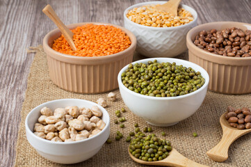 Assortment of legume products in bowls on cloth, burlap, horizontal. Healthy nutrition, vegetarianism.