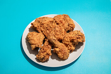 A plate of crispy fried chicken pieces placed on a neutral plate against a bright blue background, showcasing golden-brown texture and rich detail. Perfect for food photography