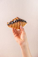 Freshly baked croissant filled with rich chocolate cream held by a hand against a soft pastel...