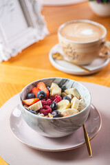 Fresh fruit bowl with assorted berries and banana served alongside a cup of coffee on a wooden table healthy eating concept