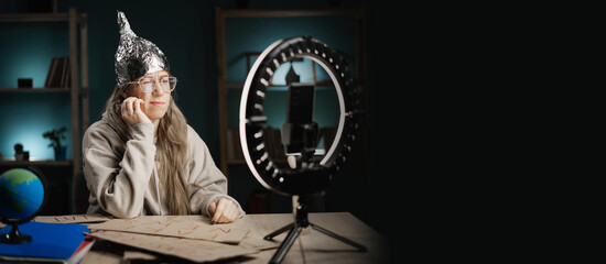 blogger conspiracy theorist in a tinfoil hat hosting a live broadcast at night at home bored with...