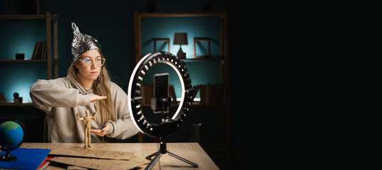 Crazy conspiracy theorist blogger woman in eyeglasses streaming live at home using smartphone and...