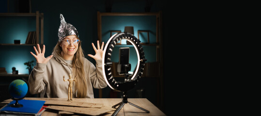 Crazy conspiracy theorist blogger woman in eyeglasses streaming live at home using smartphone and...