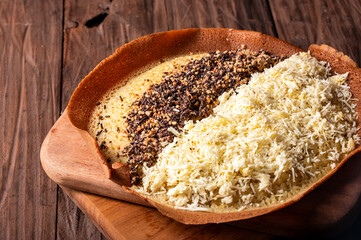 An Indonesian martabak with a crispy golden crust sits on a wooden board. It is topped with grated cheese and crushed chocolate sprinkles, against a rustic wooden background.