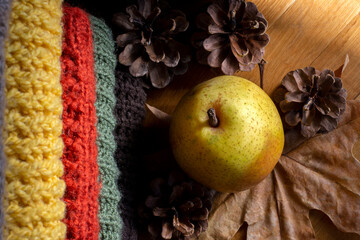 Cozy autumn still life with woolen sweaters, pinecones, leaves and pear