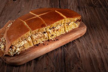 A sliced Indonesian martabak with a golden brown crust sits on a wooden board. Filled with grated cheese, chocolate sprinkles, and peanuts, against the rustic wooden background