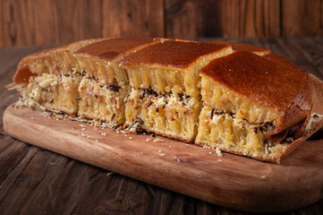A sliced Indonesian martabak with a golden brown crust sits on a wooden board. Filled with grated cheese, chocolate sprinkles, and peanuts, against the rustic wooden background