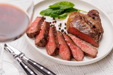 A perfectly cooked sliced striploin steak with a juicy, tender texture, served alongside a glass of rich red wine