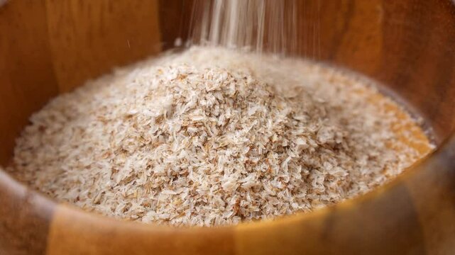 Psyllium husk (Ispaghula) falling down into a wooden bowl close up. Dietary fiber product