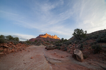 Layered sandstone is exposed in a dry ravine in the Southern Utah, USA desert below Mt. Kinesava of Zion Nat. Park. Wispy clouds fill the sky and morning's first light warms the distant cliffs.