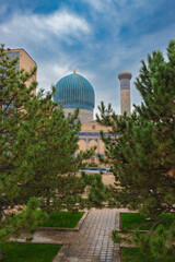 Cityscape with turquoise dome and corner tower of Sher-Dor Madrasa madrasah against green pine trees at Samarkand, Uzbekistan. Madrasah is hidden behind the foliage of the coniferous trees