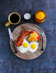 sunny side up eggs and bacon served with fresh fruit