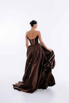 Tall brunette with hairstyle in dark brown luxurious fashionable dress with train isolated on white background