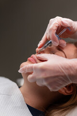 Professional cosmetologist woman giving filler injection to lip in beauty clinic. Lip augmentation...