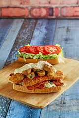 fried fish po'boy sandwich topped with fried pickles, lettuce, and tomato