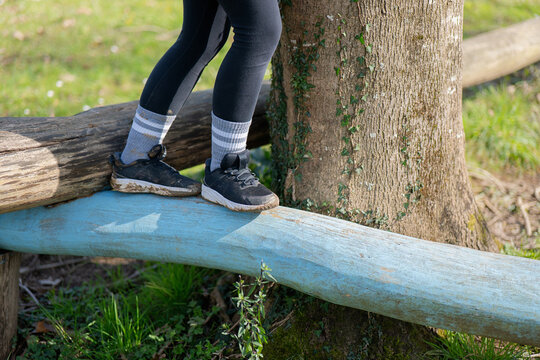 Child balances on a log in a sunny park while wearing athletic shoes and leggings