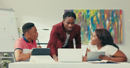 Co-workers sit at desk in office discussing gossiping about other members of company boss interrupts conversation of two friends explain errors to be corrected in project employees don't stop talking