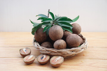 Fresh organic sapodilla fruits on basket and wooden floor. Concept, tropical fruits with soft brown peel, sweet and delicious. Agriculture crops with medicinal qualification and vitamin.              