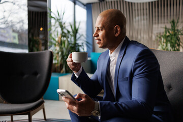 Cheerful african american businessman drinking coffee and using smartphone in hotel